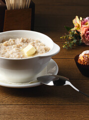 Plate of porridge with cherry jam, cake and butter on wooden table. Breakfast at the hotel, cafe, restaurant. Copy space. Morning. Food photography. Russian breakfast. Milk porridge for children. 