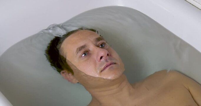 Young Man Lies Underwater in the Bath. Depression Concept and Emotional Instability. Open Eyes and Bubbles from the Mouth of Dived Man. Breath Holding