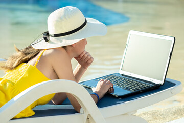 Young woman in yellow dress is laying on beach chair working on computer laptop connected to...