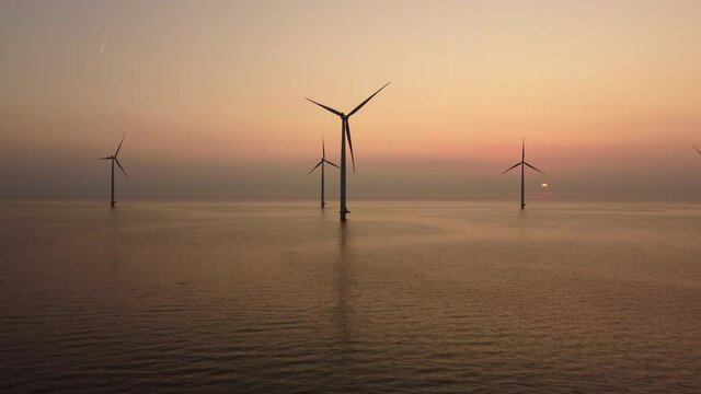 Wind turbines producing sustainable renewable electricity in an offshore wind park during sunset. Drone point of view.