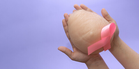 Silicone breast prosthesis on woman hands and Pink Ribbon. Breast Cancer Concept. Copy space - obrazy, fototapety, plakaty