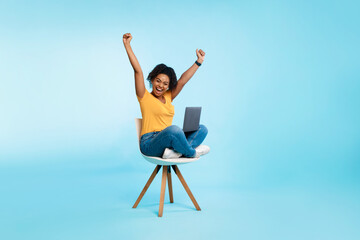 Excited young woman sitting on chair with laptop, raising hands up, screaming, winning casino bet...