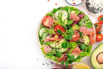 Spring salad with salted salmon, avocado, tomatoes, cucumber, black sesame seeds, olive oil, and mixed herbs. White background, top view, copy space