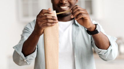 Happy african american man screwing bolt to wooden table, installing desk by yourself at home, closeup, crop