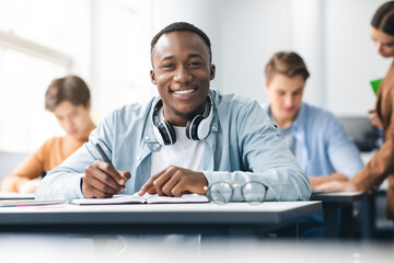 Black male student sitting at desk writing in classroom