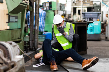 Fototapeta na wymiar First Aid. Engineering supervisor talking on walkie talkie communication while his coworker lying unconscious at industrial factory. Professional engineering teamwork concept.
