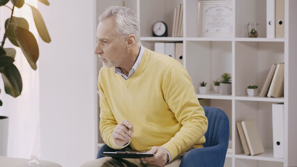 mature psychologist listening and holding clipboard during consultation