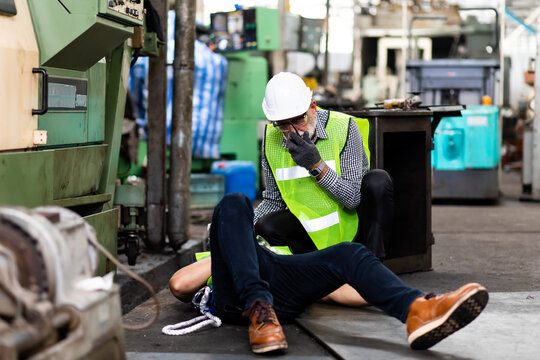 First Aid. Engineering supervisor talking on walkie talkie communication while his coworker lying unconscious at industrial factory. Professional engineering teamwork concept.