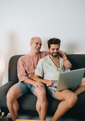 Obraz premium Gay couple sitting on sofa with laptop
