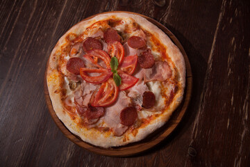 Top view shot of delicious pizza with sliced salami and ham served on wooden table
