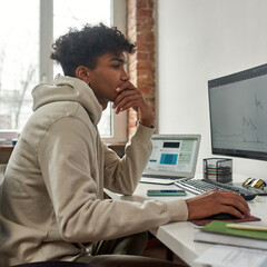 Young man looking at pc screen while trading, making money online using computer, sitting at home...