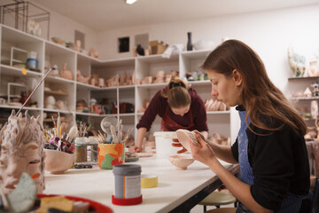 Young woman working at pottery class, glazing small bowl