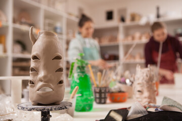 Selective focus on terracotta clay statue, female potters working at studio on background
