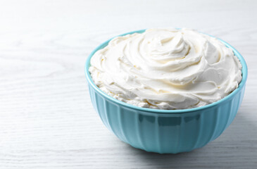 Bowl of tasty cream cheese on white wooden table, space for text