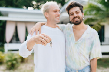 Gay couple standing and holding keys of thier new house