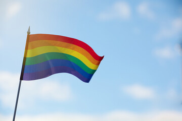 Bright LGBT flag against blue sky with clouds