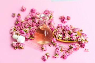 Rose  essential oil in glass bottle and pink rose flowers on pink background. Rose water 