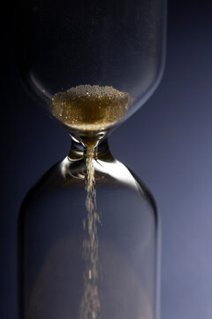 Hour Glass with running sand inside, on blue background. Time passing or countdown concept.