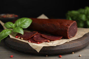 Delicious dry-cured beef basturma with basil and peppercorns on wooden table, closeup