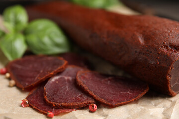 Delicious dry-cured beef basturma with basil and peppercorns on table, closeup