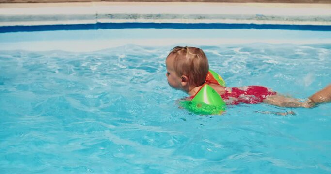 Cheerful child girl is learning to swim on swimming pool on summer vacations.Carefree childhood on holidays enjoying of fresh water