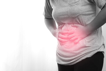 Woman wearing gray shirt has abdominal pain caused by flatulence.