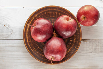 Several ripe red apples with a ceramic plate on a wooden table, close-up, top view.