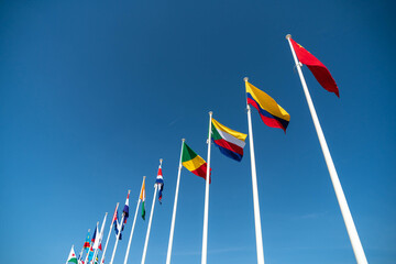 Look up view to the row of flags attached to the poles, over blue sky background, represent various countries. 