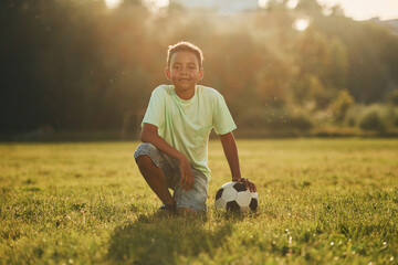 Taking a break. With soccer ball. African american kid have fun in the field at summer daytime
