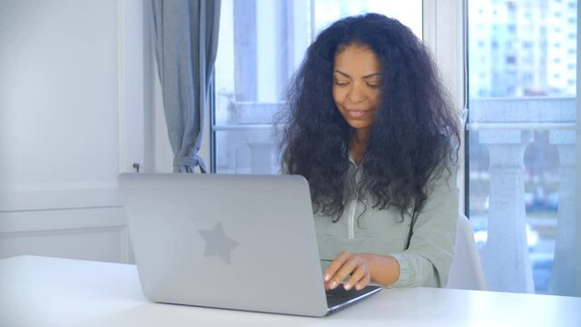 Focused young black woman working on computer. BIPOC freelancer female typing on laptop keyboard at home on lockdown. African person doing distant free lance work online with smile