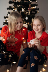 Teenage sisters in red holiday T-shirts sitting at the Christmas tree and celebrating the New Year