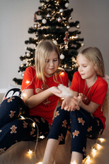 Teenage sisters in red holiday T-shirts sitting at the Christmas tree and celebrating the New Year