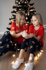 Teenage sisters in red holiday T-shirts sitting at the Christmas tree and celebrating the New Year