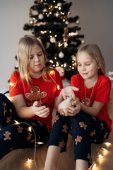 Teenage sisters in red holiday T-shirts sitting at the Christmas tree and celebrating the New Year