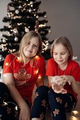 Teenage sisters in red holiday T-shirts sitting at the Christmas tree and celebrating the New Year