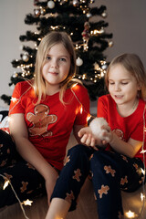 Teenage sisters in red holiday T-shirts sitting at the Christmas tree and celebrating the New Year