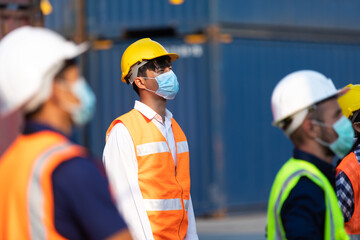 Group of professional team worker wearing protection face mask during coronavirus and flu outbreak and wearing safety hardhat helmet at container yard or cargo warehouse