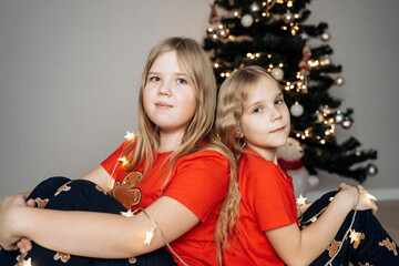 Teenage sisters in red holiday T-shirts sitting at the Christmas tree and celebrating the New Year