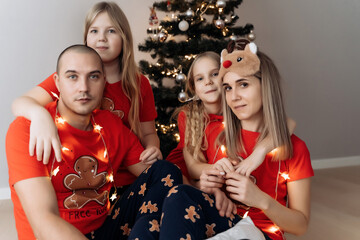 A family in red holiday T-shirts sitting at the Christmas tree and celebrating the New Year