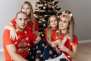 A family in red holiday T-shirts sitting at the Christmas tree and celebrating the New Year