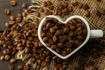 Coffee beans . Coffee beans pouring out of heart shaped cup on fabric and wooden background