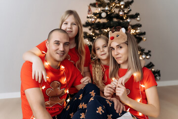 A family in red holiday T-shirts sitting at the Christmas tree and celebrating the New Year