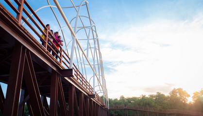 Group of Asian women in workout clothes Standing on a wooden bridge in the park in the morning when the sun rises. Wooden bridge at Chedi Klang Nam, Rayong Province, Thailand