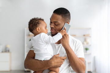 Fototapeta premium Adorable Little Black Baby Playing With Cellphone While Father Talking On It
