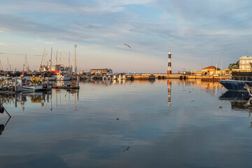 Fototapeta na wymiar The port of Cattolica with the boats and the lighthouse reflecting in the water at sunset