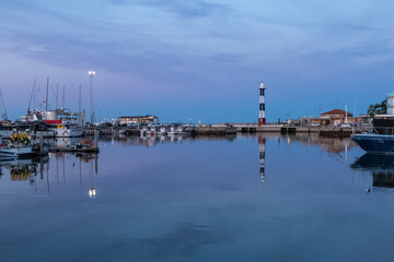 Fototapeta na wymiar The port of Cattolica with the boats and the lighthouse reflecting in the water at sunset