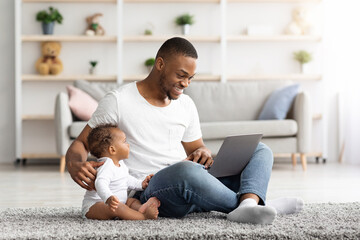 Young Black Man Working On Laptop And Taking Care About Infant Baby