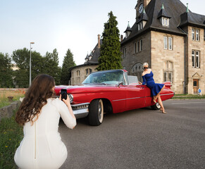 Girls take pictures of each other near a red retro car