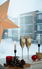 Fototapeta na wymiar Two glasses of champagne and candles on the background of snowfall outside the window