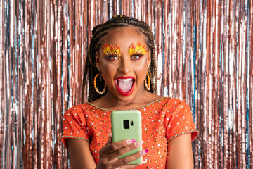 Carnival Party in Brazil, surprised black woman holding mobile on colorful background in costume